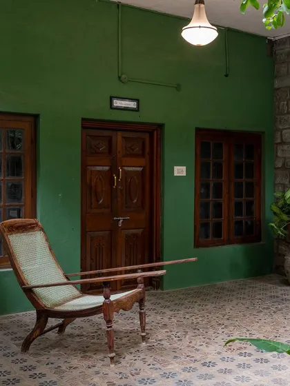 A quiet corner on the tiled patio, with a vintage planter's chair against a rich green wall, ideal for a moment of peace or a character-filled portrait.