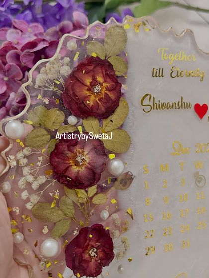 A close-up of the floral details on the engagement calendar plaque. The preserved roses and baby's breath are accented with pearls and gold flakes.