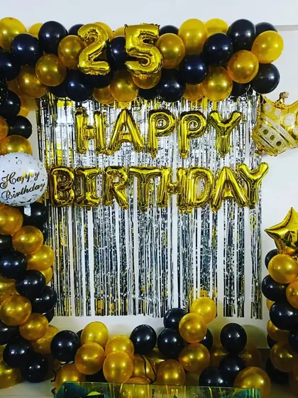 A stylish black and gold 25th birthday decoration set up in a client's home. This shows a full balloon arch framing the wall, with foil number balloons and a crown prop for a royal touch.