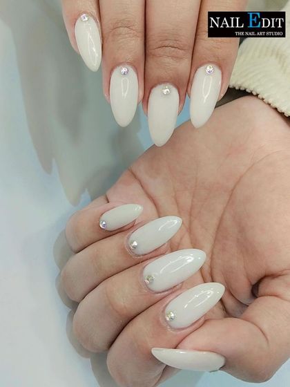 A simple yet incredibly elegant look. These milky white almond-shaped nails are each adorned with a single, perfectly placed rhinestone at the cuticle for a touch of minimalist sparkle.