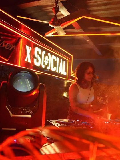 A DJ in her element at the Social Sunday Sundowner, surrounded by red neon lights and smoke.