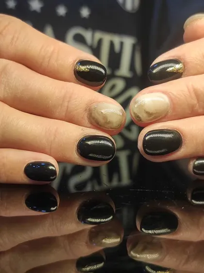 A chic black manicure with marbled accent nails featuring a touch of gold.