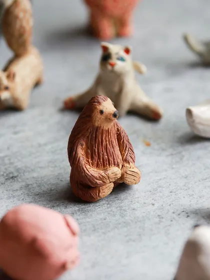 A furry looking sloth, sculpted with intricate texture, sits among other miniature creations from our animal workshop.