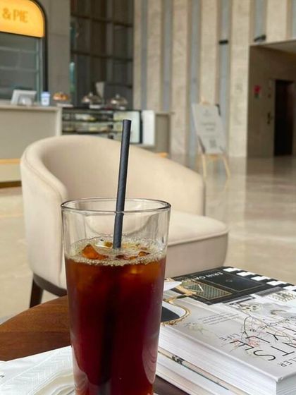 A refreshing glass of iced coffee sits on a table next to a book, the perfect companion for a quiet afternoon at our Bellandur cafe.