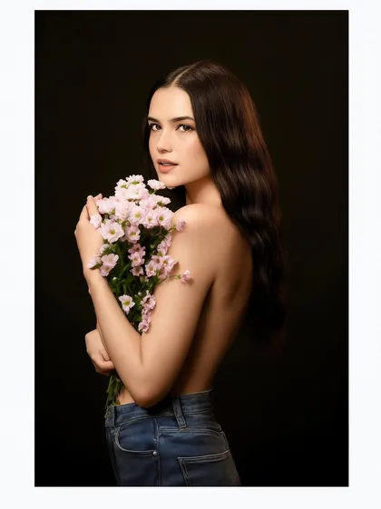 A delicate and minimalist portrait of a model holding a bouquet of flowers, shot against a clean black background.