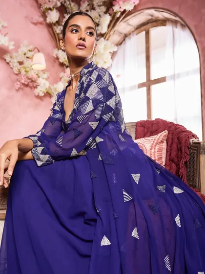 A seated portrait in a deep blue ensemble. The makeup is elegant and understated, with a focus on a flawless complexion and softly defined eyes.