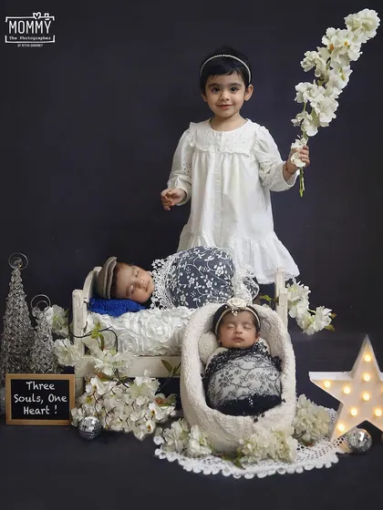 "Three souls, one heart." This photo captures the sweet bond between an older sister and her newborn twin siblings in a lovely white and silver themed setup.