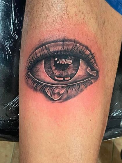 A realistic eye tattoo with a teardrop on the inner arm.