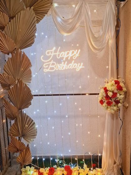 A close-up of the balcony decoration, showing the neon sign, fairy lights, and dried palm leaves for a bohemian-chic birthday vibe.