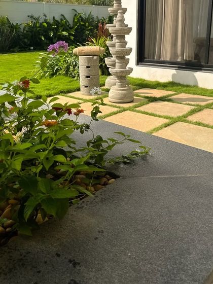 We believe in blending tradition with modern design. Here, a stone deepam stands among flowering shrubs and a checkerboard lawn, adding a touch of cultural heritage to the landscape.