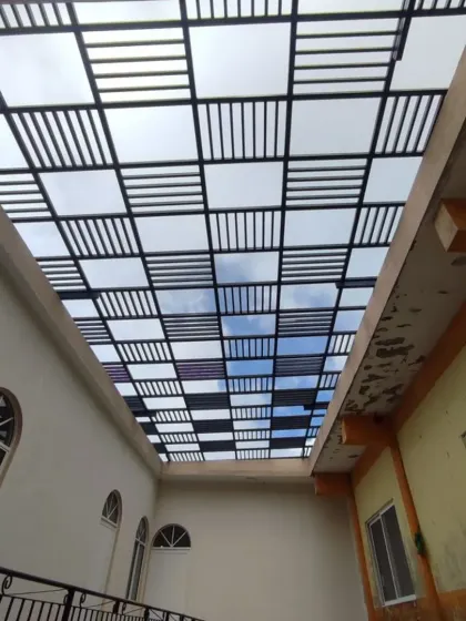 A view from below a complex rafter and polycarbonate roof during installation. The grid-like pattern creates a modern, industrial aesthetic while providing both shade and light.