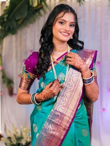 A radiant bride in a turquoise and purple saree, smiling for the camera.
