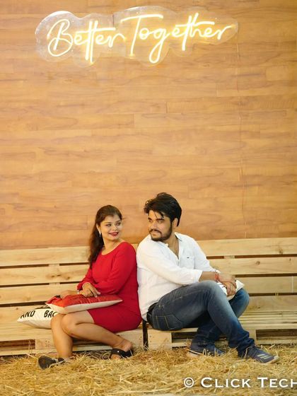 A cute shot of a couple sitting back-to-back on a rustic wooden bench, with a 'Better Together' neon sign above them.