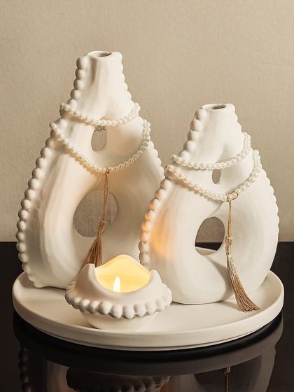 This serene white decorative set brings a feeling of Zen to your home. The unique, abstract shapes of the vases and the small candle holder create a calm and peaceful tabletop arrangement.