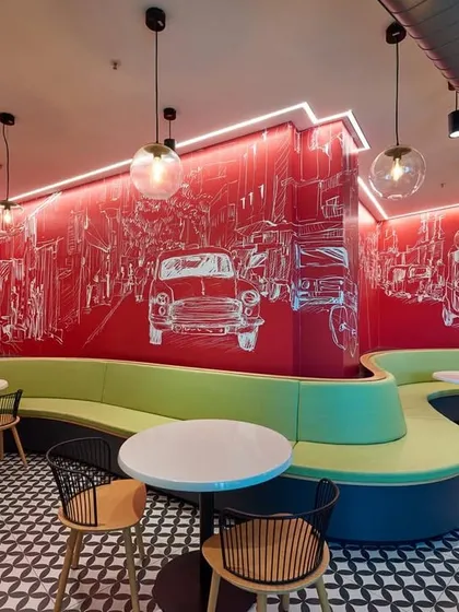 Another view of the large cafeteria, showing the flowing lines of the seating and the dynamic red wall mural that wraps around the space.