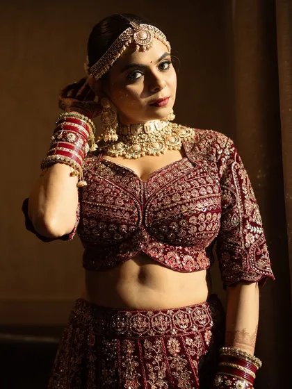 A powerful portrait of the bride in her deep red velvet lehenga. The dramatic lighting highlights her sculpted features and the rich texture of her outfit.