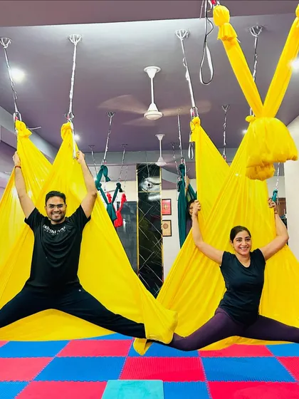 Partner aerial yoga is a great way to connect and build trust. These two students work together to create a beautiful and balanced split pose using the bright yellow hammocks.