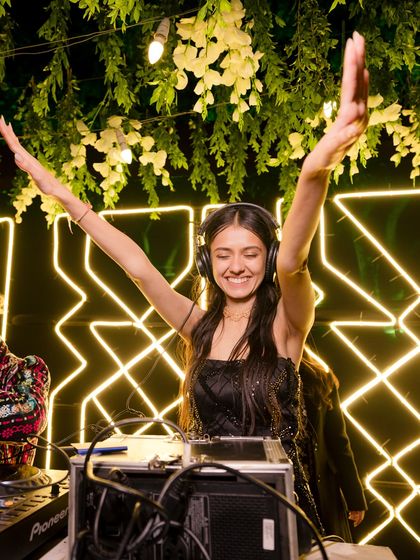 The bride taking over the DJ console, her hands in the air, embodying the fun and carefree spirit of the evening.