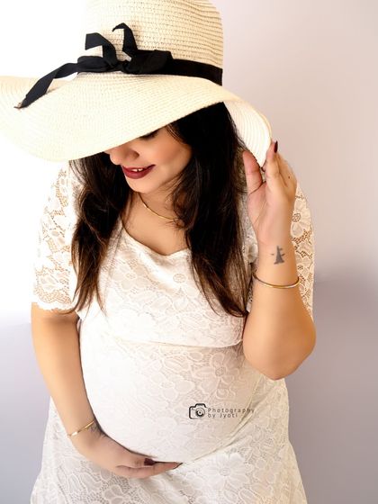 A chic and stylish maternity shot. The mom-to-be wears a white lace dress and a sun hat for a casual yet elegant look.