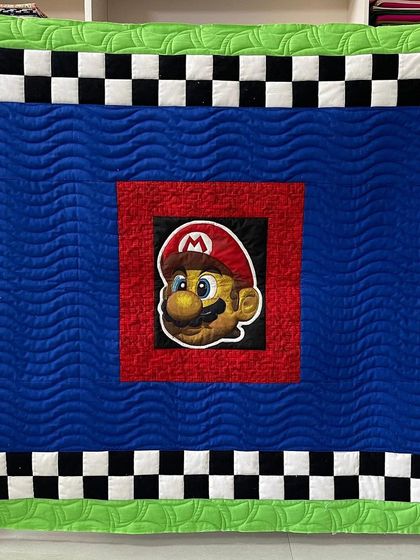 It's-a-me, Mario! This Super Mario themed quilt is perfect for any young gamer, featuring a large appliqué of Mario's face, a checkerboard border, and wavy quilting to mimic movement.