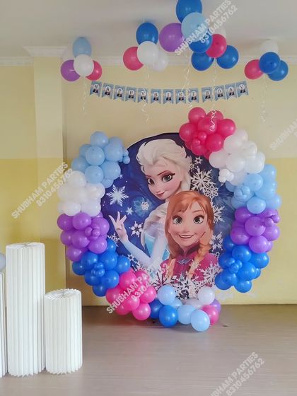 A complete Frozen party setup with a character backdrop, balloon garland, and themed cake stands.