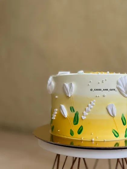 A close-up of a cake with a yellow ombre effect and delicate, hand-painted white flowers.