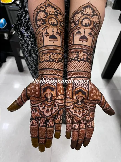A detailed look at a symmetrical bridal design. The arms feature elephants and hanging jhumkas, while the palms have a unique, ornate pattern.