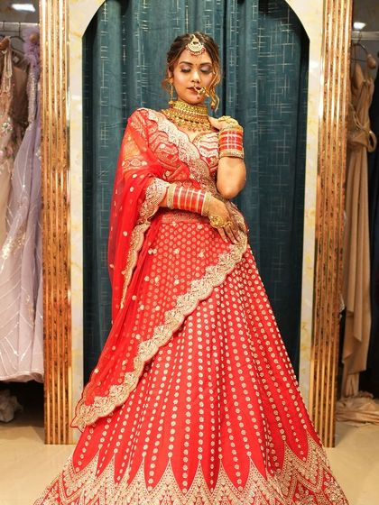 A full-length view of a bride in a stunning red lehenga. The outfit features beautiful patterns and a flattering A-line cut, making it a comfortable yet glamorous choice.