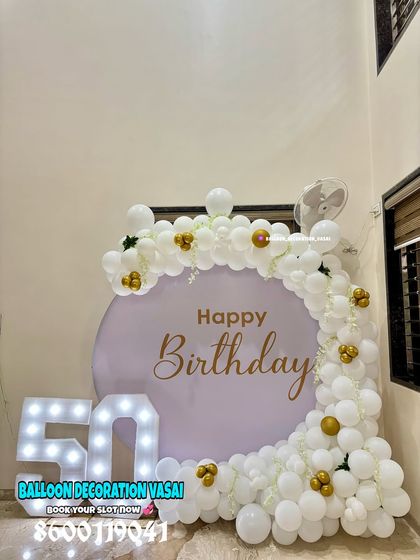 A clean and elegant 50th birthday decoration. The white balloon arch with gold accents on a lavender backdrop creates a sophisticated look.