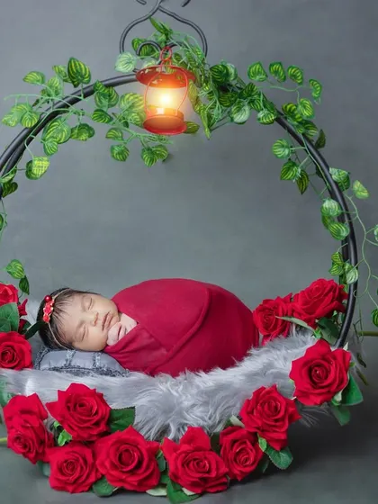 A dreamy setup with a newborn sleeping in a hanging wreath adorned with red roses.