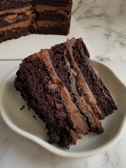 A close-up of my signature Decadent Belgian Chocolate cake. This slice shows the incredibly moist, multi-layered sponge and rich, melt-in-your-mouth chocolate mousse that makes it a crowd favorite.
