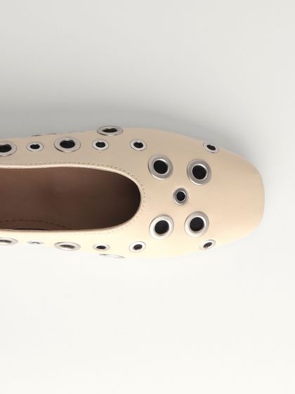 A close-up of the eyelet ballet flats in a soft cream leather. This design plays with negative space, making it a statement piece that remains a versatile staple for any wardrobe.