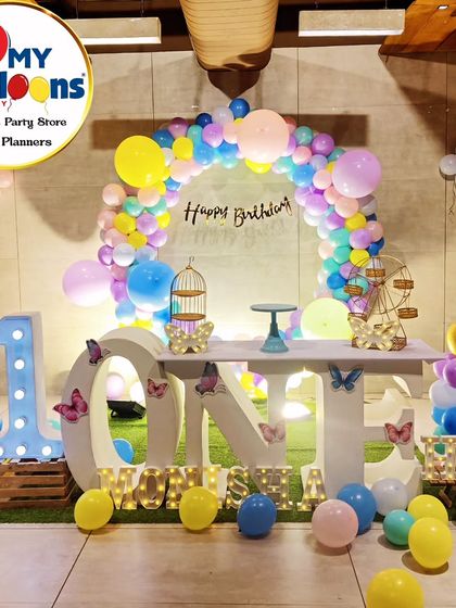 A colorful butterfly-themed first birthday. The setup includes a 'ONE' marquee table, a rainbow balloon arch, and butterfly accents.