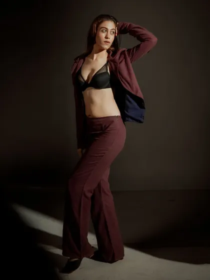 A full-length studio shot demonstrating how lighting can define a space. The sliver of light on the floor grounds the model, drawing attention to her confident stance and the flow of the wide-leg trousers.