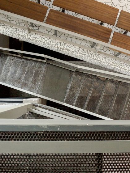 An overhead view of the staircase in the Artrovert studio, highlighting the industrial aesthetic of the steel armature and perforated metal, contrasted with the patterned tile flooring.