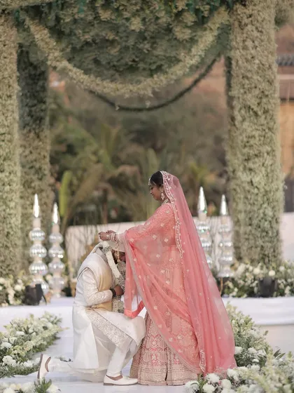 A moment of tradition and love as the bride places the garland on her groom. The elegant white and green floral decor provides a serene and beautiful setting for this important ritual.