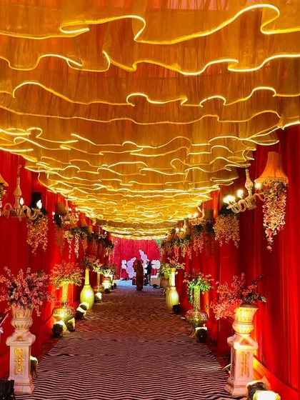 A view from inside a dramatic red and gold entrance tunnel. The ceiling is made of ruffled golden fabric with lights, while the walls are draped in rich red velvet.