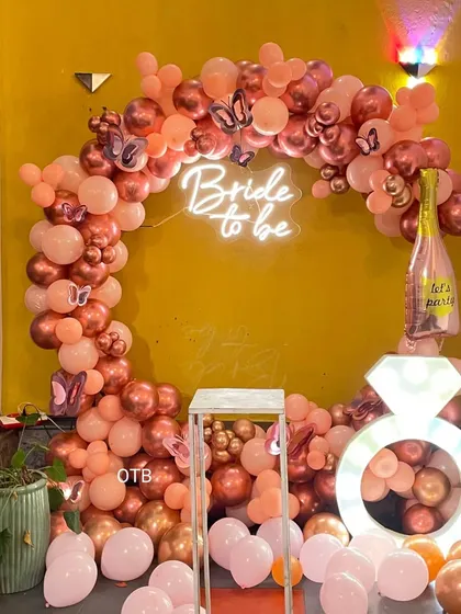 A beautiful rose gold theme for a bachelorette party. This balloon arch is accented with butterfly details, a 'Bride to be' neon sign, and the light-up ring prop for extra glam.