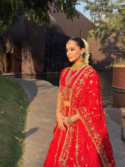 A full-length view of a traditional red lehenga, glowing in the sunlight. The styling includes a beautifully draped dupatta that adds to the grandeur of the outfit.