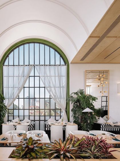 Looking out through the grand arched window at Brassa, which floods the dining area with natural light. The design incorporates abundant greenery, blurring the line between the indoor and outdoor spaces.