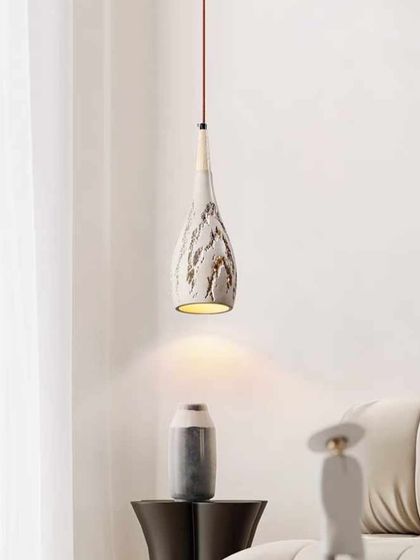 A single textured ceramic pendant in a living room setting. Its organic shape and finish complement a soft, minimalist decor style.