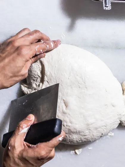 The process of making bread by hand is something I find deeply therapeutic. Here, I'm shaping fresh dough for our house-made ciabatta, ensuring every loaf has the perfect texture and flavor.