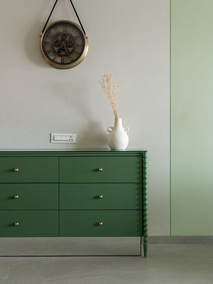 Minimalism can make a powerful statement. This simple green chest of drawers with delicate brass knobs, paired with a vintage-style clock, creates a corner that is clean, stylish, and functional.