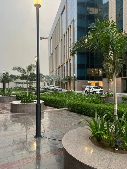 The same corporate campus viewed on a rainy day, showcasing the durability and year-round beauty of our landscape designs. The wet pavement reflects the ambient lighting and lush greenery, creating a tranquil scene.