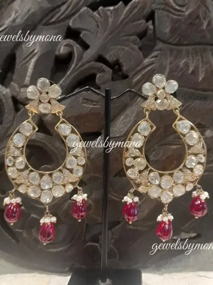 A variation of the classic polki chandbali earrings. This pair features a floral stud and delicate ruby drops, adding a touch of color and femininity to the traditional design.