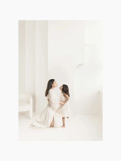 A mother and daughter share a moment of quiet communication in a minimalist all-white studio. This image is about the laughter and lessons shared across a lifetime of memories.