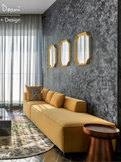 Another view of the living room, featuring a long yellow sofa against a dark, textured wall. The geometric mirrors add a touch of art deco glamour to the space.