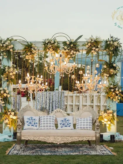 A beautiful seating arrangement for a Mehendi-Sangeet, with a regal sofa, block-printed cushions, and a backdrop of chandeliers and flowers.