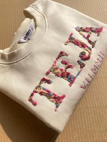 A different angle of the 'TEJA' sweatshirt, showing the intricate details of the flowers that make up each letter.