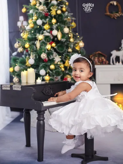 Even after Christmas, the celebration continues. A little girl in a white dress plays a tune on a mini piano by the tree.